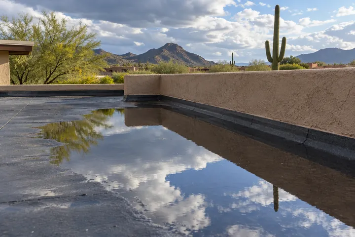 Rainwater standing on a flat roof beside a stucco parapet
