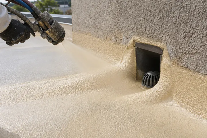 Fresh spray foam being applied around a parapet scupper